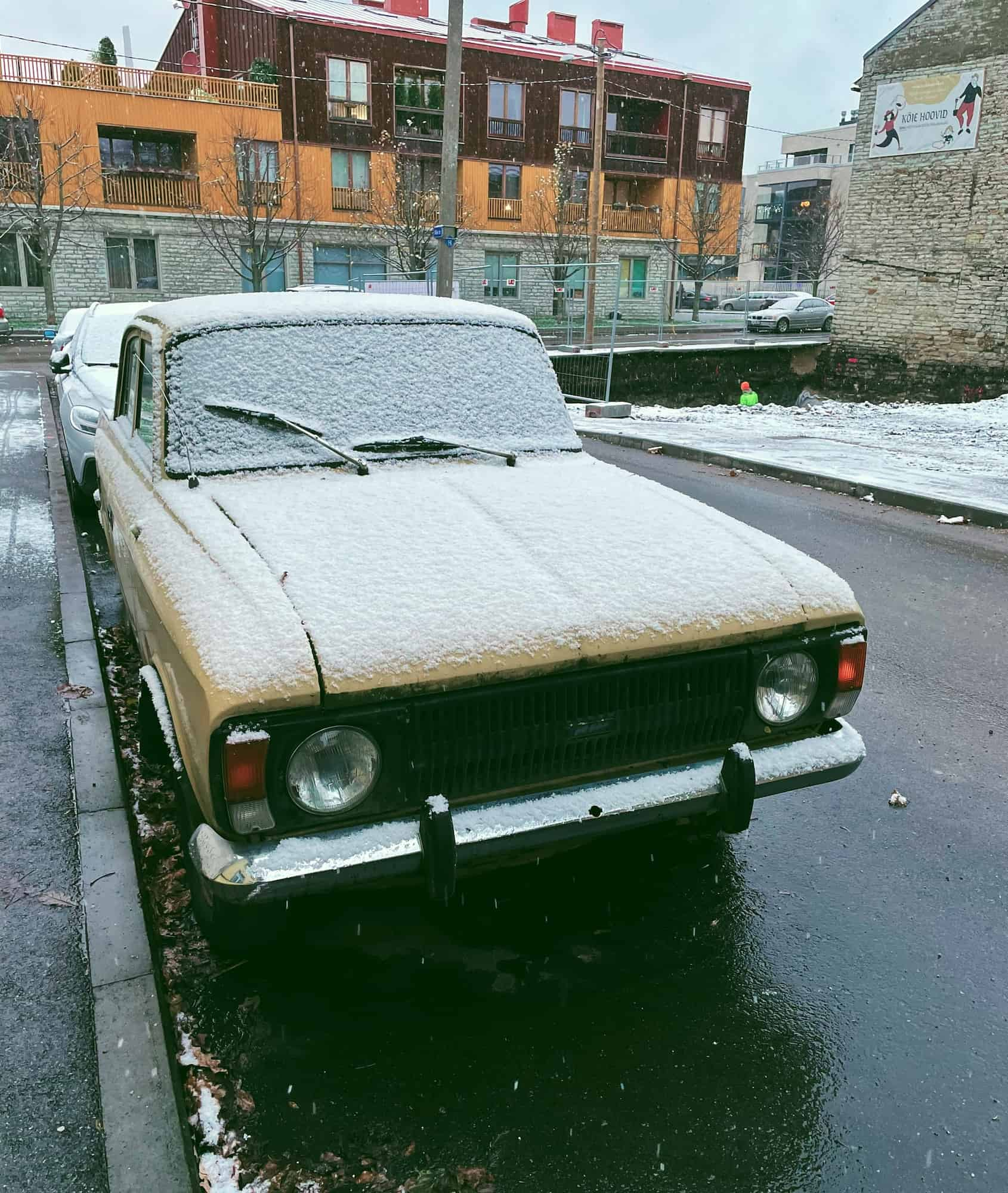 Car in Estonia parked at the roadside, partially covered in snow. Parking paid via mobile